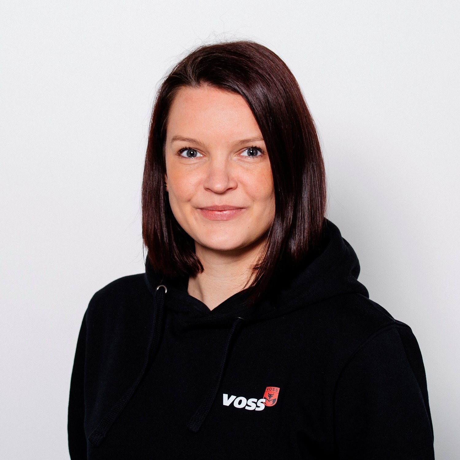 Eine Frau mit schulterlangen, braunen Haaren lächelt freundlich in die Kamera, während sie einen schwarzen Hoodie trägt.