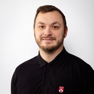 Professionelles Porträt eines lächelnden Mannes in Schwarz Ein Mann mit einem freundlichen Lächeln trägt ein schwarzes Poloshirt mit einem roten Logo auf der linken Brustseite.