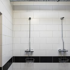 Ein modernes Duschbad mit weißen Fliesen und zwei Duschköpfen, die an der Wand montiert sind, bietet eine saubere Atmosphäre.