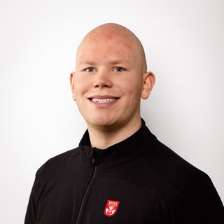 Porträt eines freundlichen Mannes mit Glatze und lächelndem Gesicht Ein junger Mann mit Glatze lächelt freundlich in die Kamera, trägt einen schwarzen Reißverschluss-Pullover mit einem Logo.