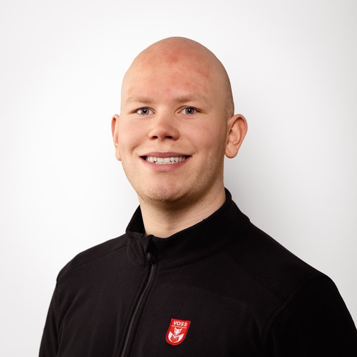 Ein junger Mann mit Glatze lächelt freundlich in die Kamera, trägt einen schwarzen Reißverschluss-Pullover mit einem Logo.