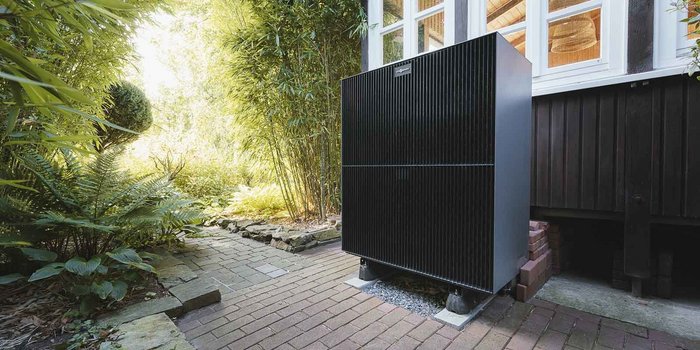 Ein schwarzer, moderner Kühlschrank steht in einem üppigen Garten, umgeben von grünen Pflanzen und einem gepflasterten Weg.