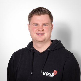 Porträt eines jungen Mannes mit freundlichem Ausdruck Ein junger Mann mit kurzem, blondem Haar lächelt freundlich in die Kamera, während er einen schwarzen Hoodie trägt.