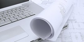 Ein Laptop steht auf eine Technische Zeichnungen und darauf ist eine Zeichnung eingerollt