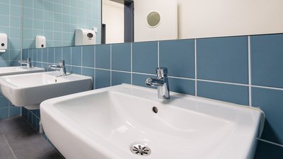 Zwei moderne Waschbecken mit glänzenden Wasserhähnen vor einer blauen Fliesenwand in einem hellen Badezimmer.