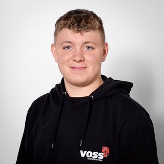 Porträt eines lächelnden Teenagers in schwarzem Sweatshirt Ein junger Mann mit lockigem Haar trägt einen schwarzen Hoodie mit dem Logo von VOSS und lächelt freundlich in die Kamera.