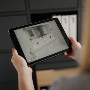 Eine Person hält ein Tablet, das eine moderne Badezimmeransicht mit eleganten Armaturen und einem großen Spiegel zeigt.
