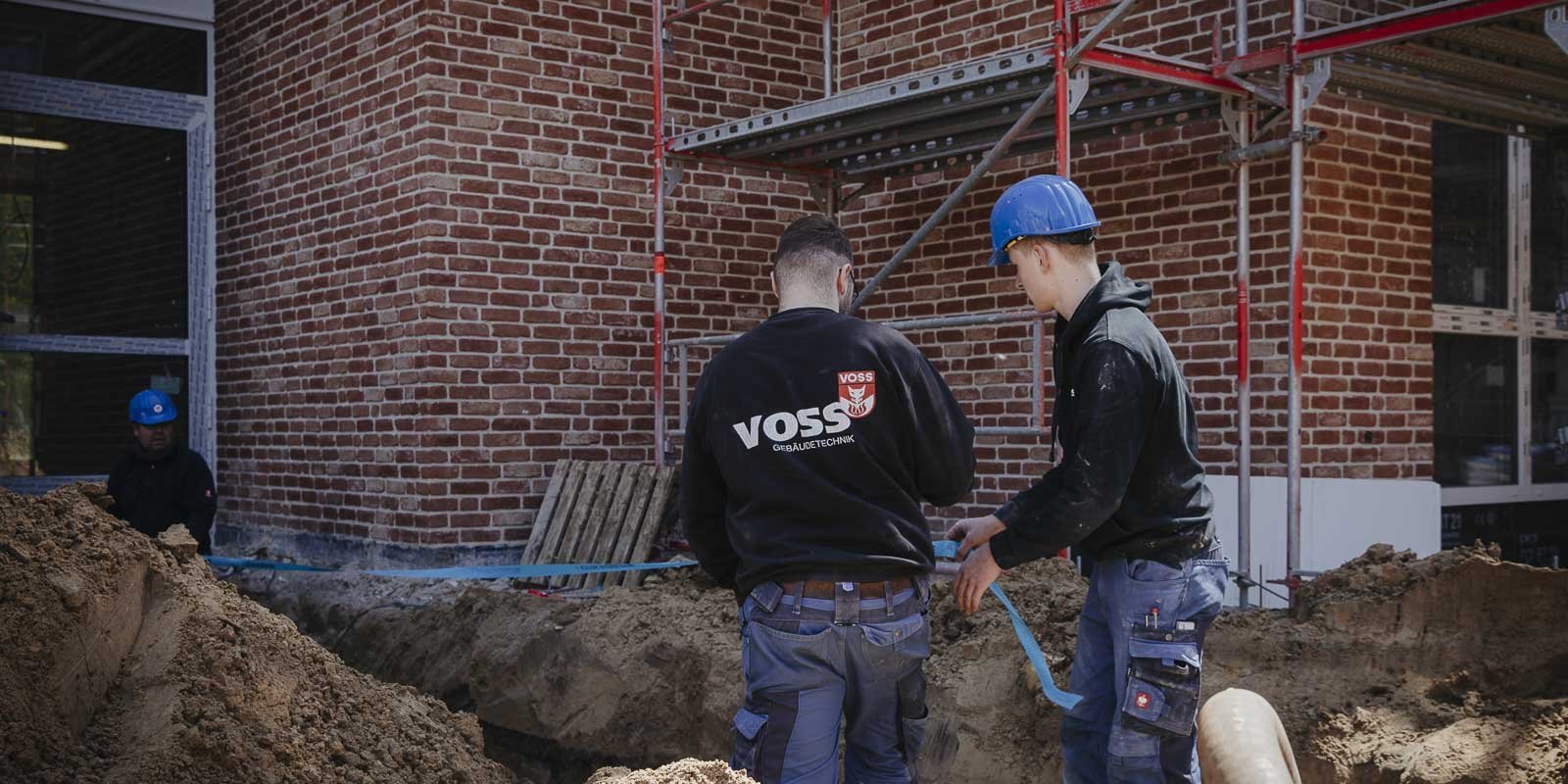 Zwei Bauarbeiter in blauen Helmen arbeiten an einem Bauprojekt, während sie eine Schaufel in der Hand halten.