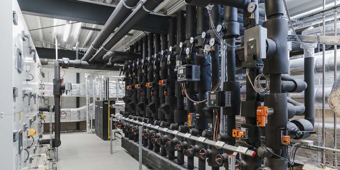 Ein industrieller Raum mit zahlreichen schwarzen Rohren und Ventilen, die an Wänden und Decken montiert sind.