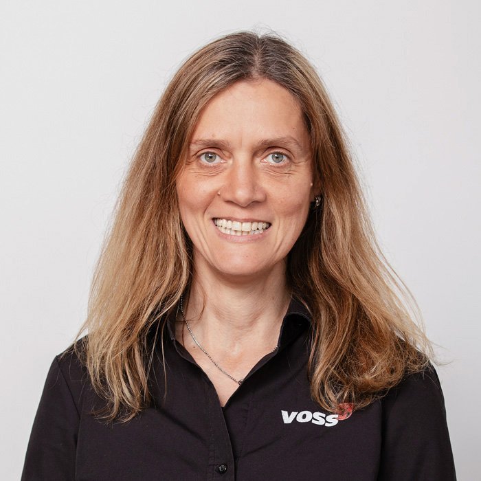 Eine Frau mit langen, blonden Haaren lächelt freundlich in die Kamera, trägt ein schwarzes Hemd mit dem Logo von VOSS.