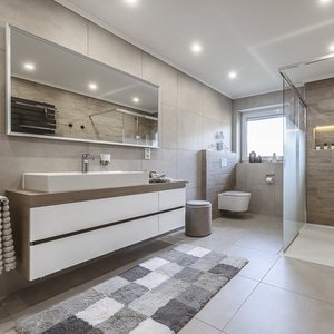 Ein modernes Badezimmer mit einem großen Spiegel, einer eleganten Waschtischkombination und einer Dusche aus Glas.