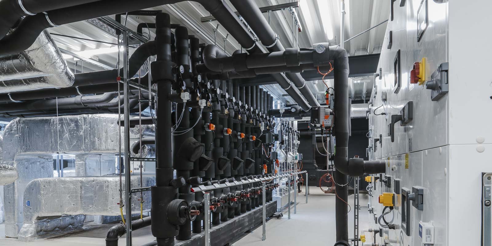 Ein modernes Technikraum mit zahlreichen Rohren und Ventilen, die an Wänden und Decken montiert sind, sorgt für eine industrielle Atmosphäre.