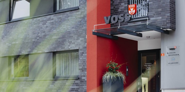 Die moderne Fassade eines Gebäudes mit dem Schriftzug 'VOSS' und einer auffälligen roten Wand im Vordergrund.