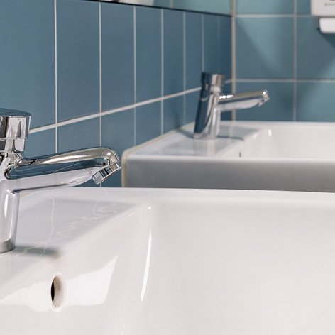Zwei moderne Waschbecken mit glänzenden Wasserhähnen vor einer blauen Fliesenwand, die eine saubere Atmosphäre schaffen.