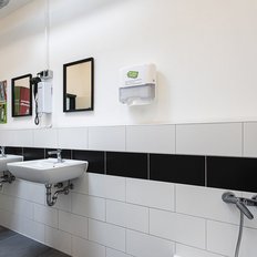 Ein modernes Badezimmer mit zwei Waschbecken, einem Handtuchspender und einem Werbeaufsteller für Pflegeprodukte.