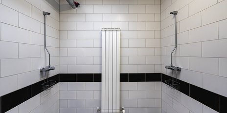 Ein modernes Duschbad mit weißen Fliesen und einem Heizkörper in der Mitte, umgeben von zwei Duschköpfen.