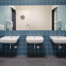 Ein modernes Badezimmer mit blauen Fliesen, drei Waschbecken und einem großen Spiegel, der die Sauberkeit betont.