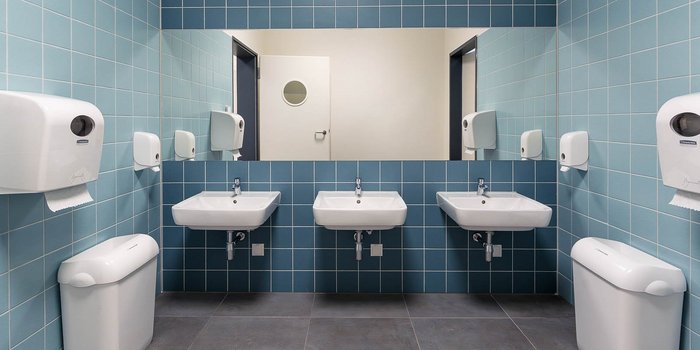 Ein modernes Badezimmer mit blauen Fliesen, drei Waschbecken und einem großen Spiegel, der die Sauberkeit betont.