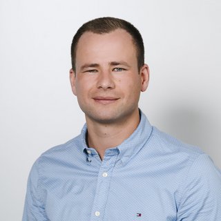 Professionelles Porträt eines jungen Mannes mit lässigem Stil Ein junger Mann mit kurzem Haar lächelt freundlich in die Kamera, während er ein hellblaues Hemd trägt.