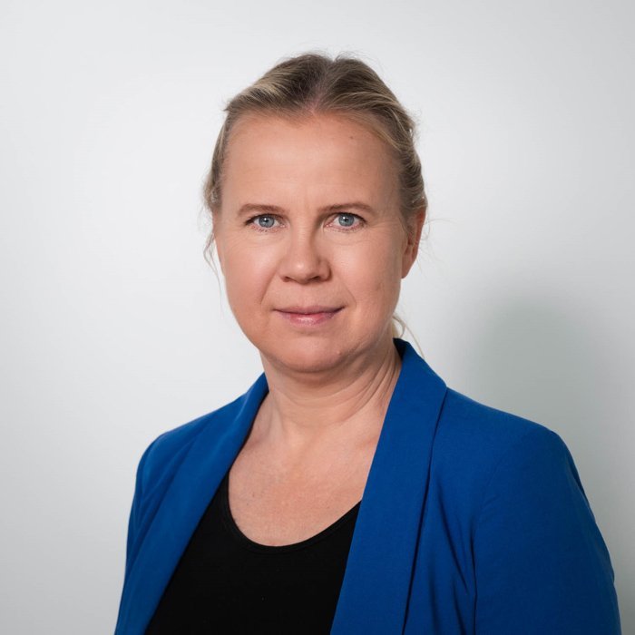 Eine Frau mit blonden Haaren trägt einen blauen Blazer und schaut direkt in die Kamera, mit einem neutralen Gesichtsausdruck.