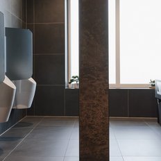 Ein modernes Herren-WC mit eleganten Urinalen und einem stilvollen Waschbeckenbereich, umgeben von dunklen Fliesen.