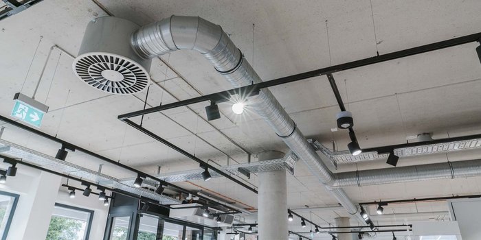 Die Decke eines modernen Raumes mit sichtbaren Lüftungsrohren und mehreren Deckenleuchten, die eine helle Atmosphäre schaffen.