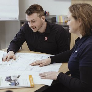 Ein Mann und eine Frau betrachten gemeinsam einen großen Plan auf einem Tisch, während sie angeregt diskutieren.