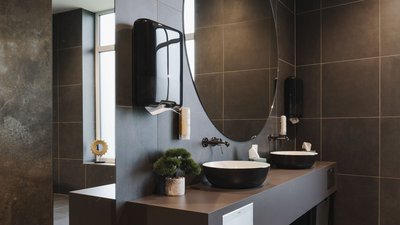 Ein modernes Badezimmer mit einem eleganten Waschbecken und einem großen Spiegel, umgeben von stilvollen, dunklen Fliesen.