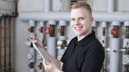 Ein Anlagenmechaniker vor einer Heizungsanlage mit einem Tablet