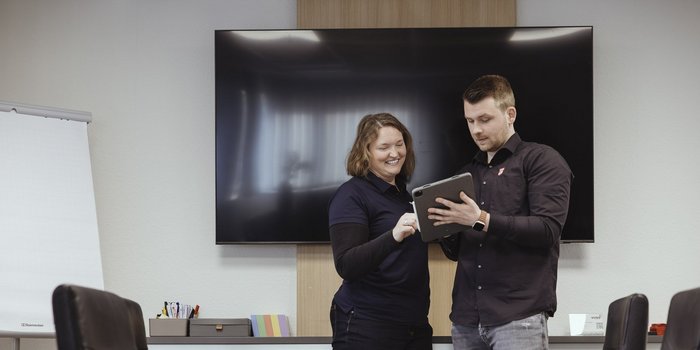 Ein Mann und eine Frau stehen in einem modernen Besprechungsraum und schauen gemeinsam auf ein Tablet.