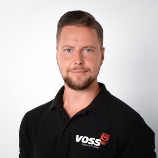 Professionelles Porträt eines Mannes in schwarzem Poloshirt Ein Mann mit einem gepflegten Bart trägt ein schwarzes Poloshirt mit dem Logo von VOSS Gebäude-Technik.