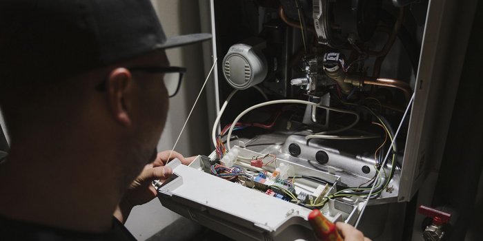 Ein Techniker untersucht sorgfältig die Innenteile eines Heizgeräts, während er mit einem Schraubendreher arbeitet.