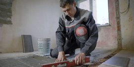 Ein Fliesenleger der mit einer Wasserwaage die Fliesen ausrichtet